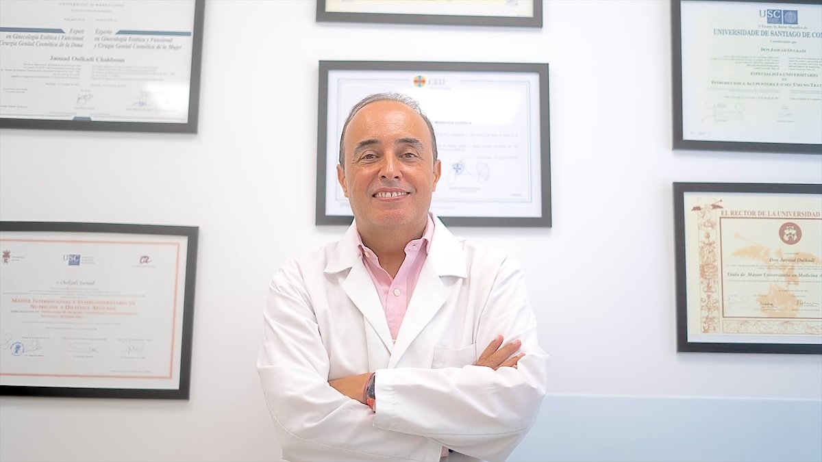 Dr. Jaouad Oulkadi con bata blanca ante la pared de diplomas de su clínica